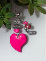 A vibrant pink heart tagua carved bag charm with glossy finish and Tibetan heart amulet metal bead keychain