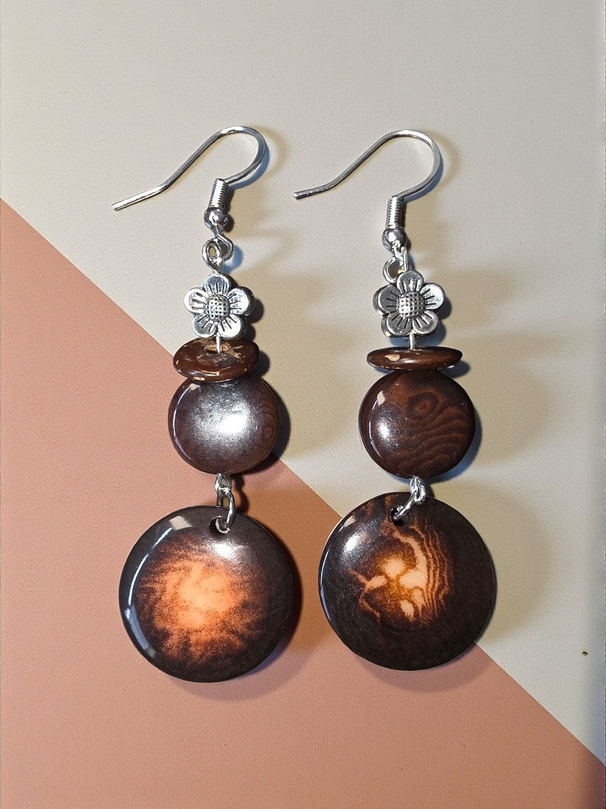 Pair of earrings with brown beads and silver floral accents on a two-tone background.