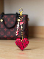 A vibrant red and black marbled carved heart tagua charm hanging from a gold-toned chain for bag or keychain use
