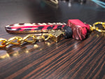 A vibrant pink and black marbled tagua heart keychain with a gold chain zebra print blade and starburst charms
