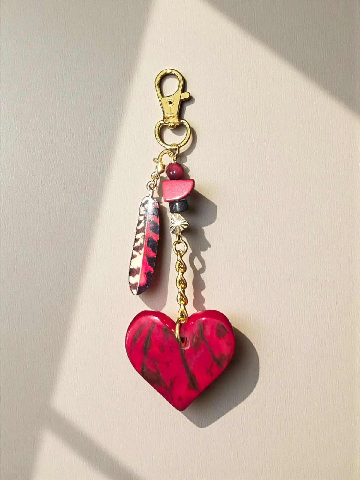A vibrant red and black marbled heart tagua charm with gold chain for bags or keychains