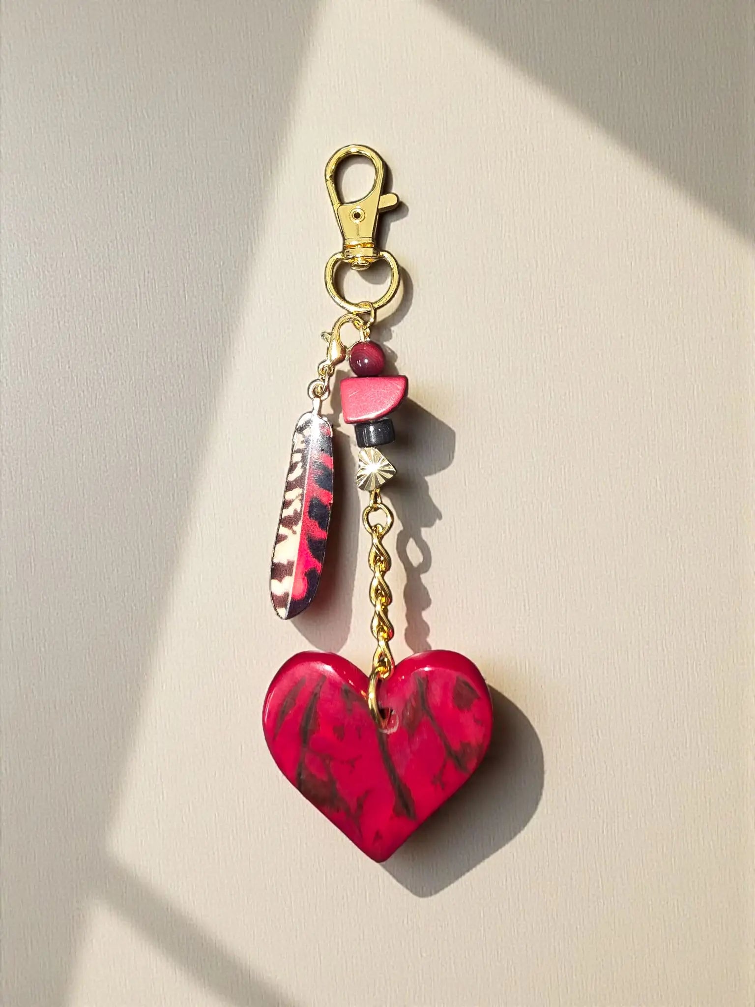 A vibrant red and black marbled heart tagua charm with gold chain for bags or keychains