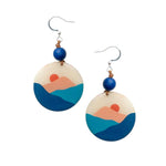 Mauren earrings circular tagua nut hand-painted with layered blues and peachy-orange hills and a vibrant blue bead