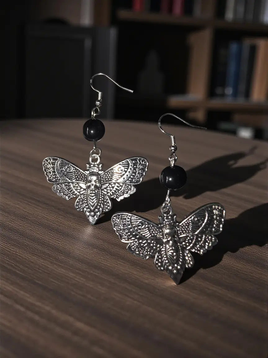 Silver butterfly earrings with intricate filigree and skull motif accented by black tagua nut beads above wings