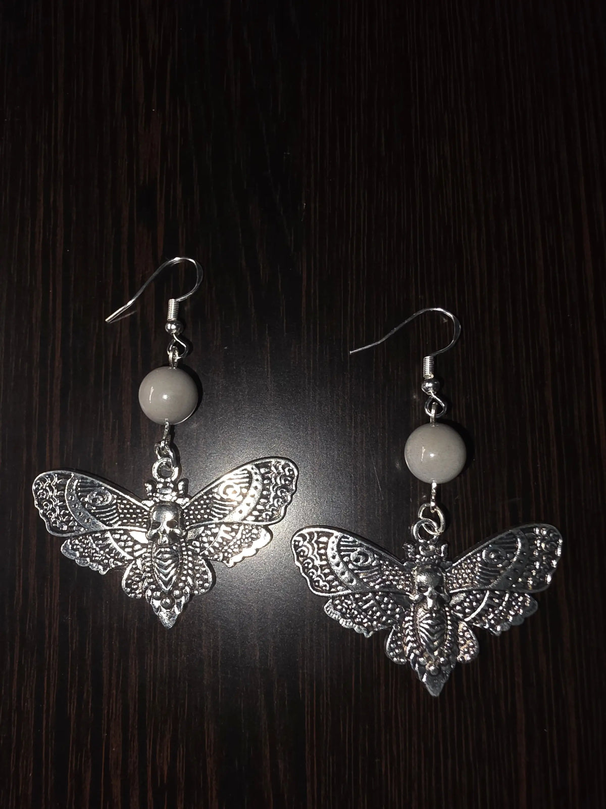 Silver butterfly earrings with intricate filigree skull motif hanging from gray tagua nut beads