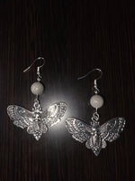 Silver butterfly earrings with intricate filigree skull motif hanging from gray tagua nut beads