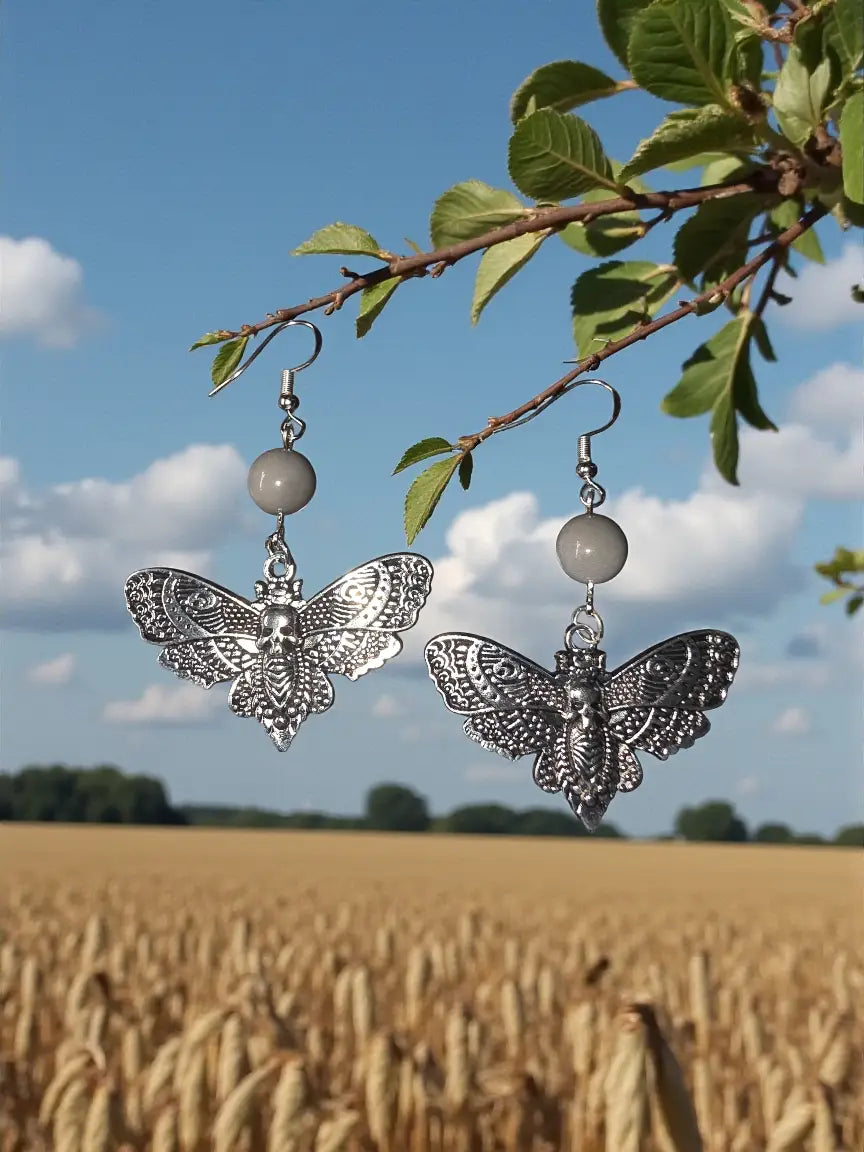 Silver butterfly earrings with intricate lace wings and skull design hanging from round gray tagua nut beads