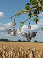 Silver butterfly earrings with intricate lace wings and skull design hanging from round gray tagua nut beads