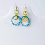 A pair of mona drop and dangle circle statement tagua earrings with bright yellow and translucent turquoise rings