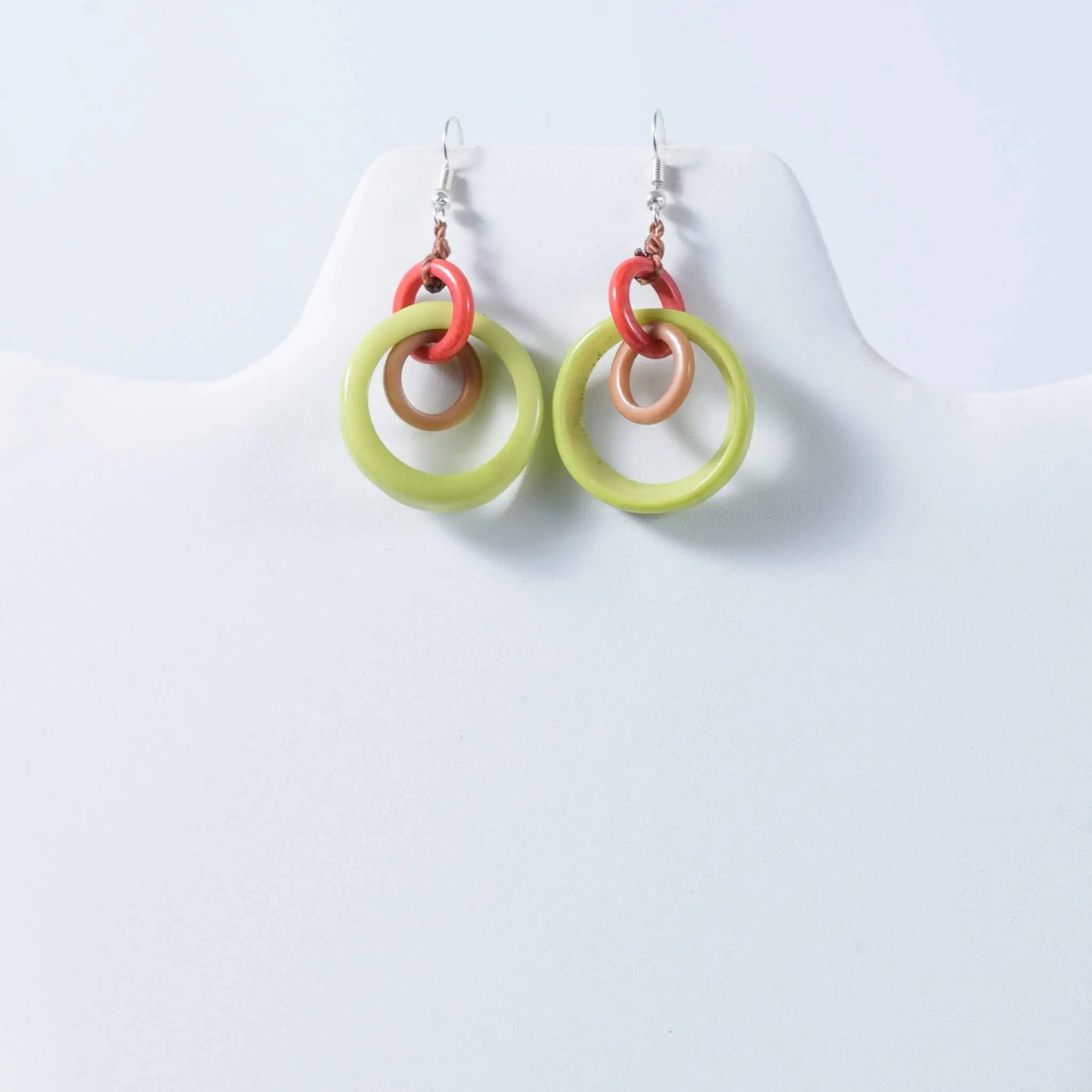 A pair of mona drop and dangle circle statement tagua earrings with lime green, coral red, and tan layered rings