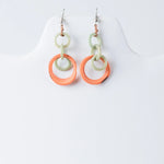 A pair of mona drop and dangle circle tagua earrings in bold orange and mint green with glossy resin finish