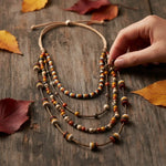 Sun & Wing Studio bohemian multi-strand layered necklace with mustard, orange, and grey beads on a rustic wooden table.