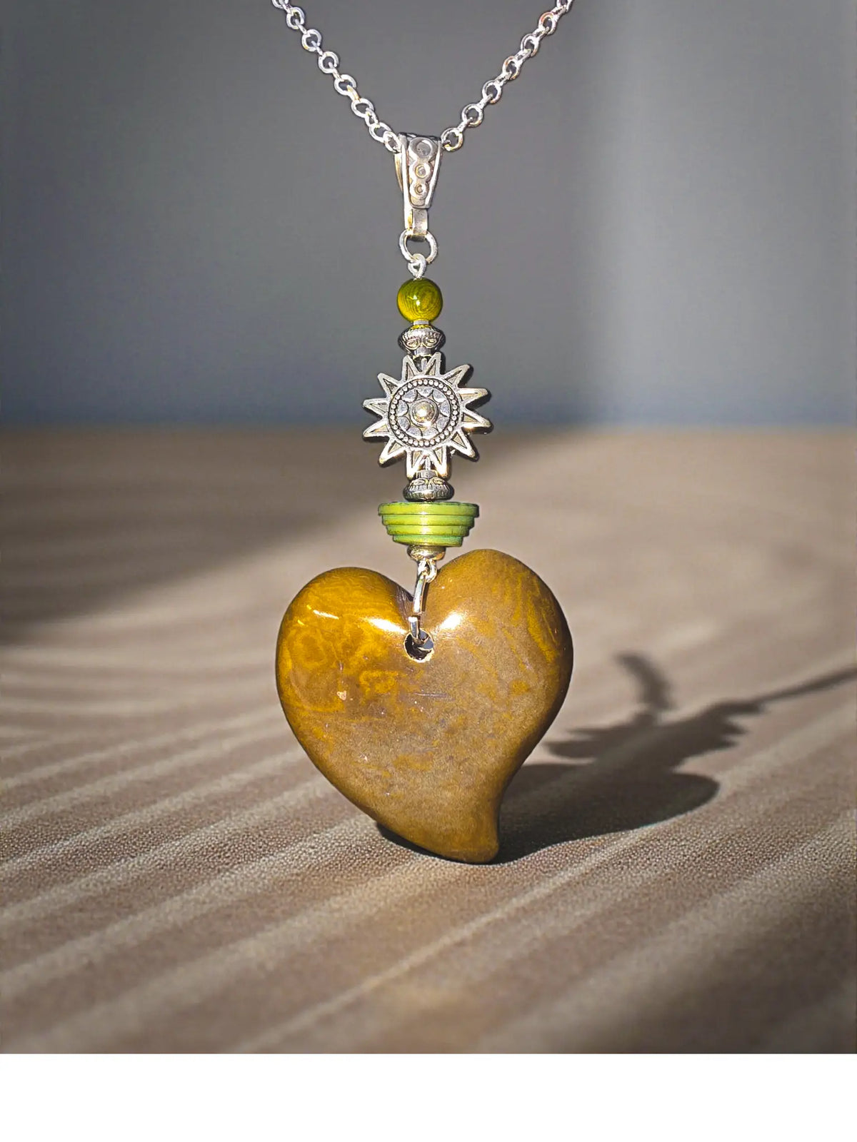A polished golden-brown olive carved heart pendant with sun amulet charm and green beads on silver chain necklace