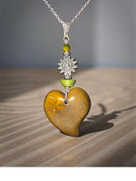 A polished golden-brown olive carved heart pendant with sun amulet charm and green beads on silver chain necklace