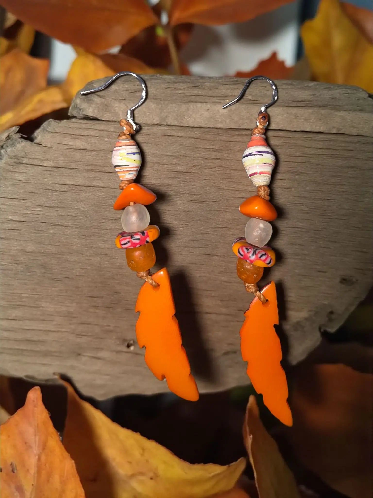 Orange crush carved tagua leaf drop earrings featuring orange feather-shaped dangles with paper-wrapped beads and metallic hooks