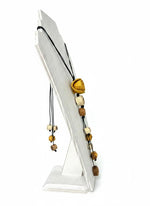 A dainty eco friendly necklace made with cream tan dark brown wooden beads and a golden bell shaped orange peel pendant