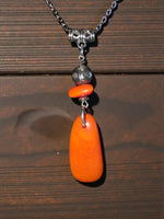 A vibrant orange amber pendant with a ladybug bead on a silver chain features fair trade craftsmanship from the rainforest