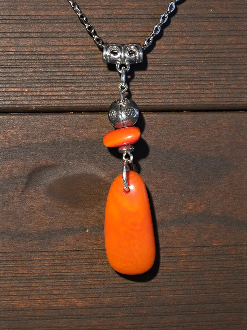 A vibrant orange amber pendant with a ladybug bead on a silver chain features fair trade craftsmanship from the rainforest