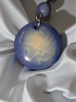 Periwinkle tagua round disc earrings with glossy blue and creamy white swirls suspended from purple bead on gold chain
