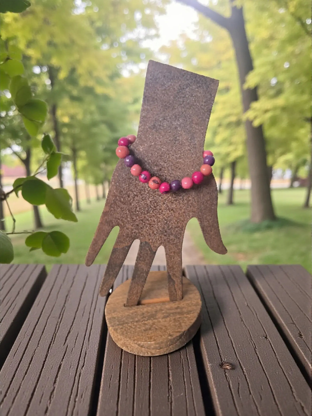 A vibrant pink and purple pink forest pambil seed bracelet displayed on a rustic metal hand stand fair trade from ecuador