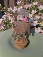 Pink floral-patterned leather watch band on wooden hand stand paired with pink marble natural edge seed bracelets