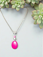 A vibrant pink tagua necklace with an oval pendant silver chain and fair trade heart bead charm from the rainforest