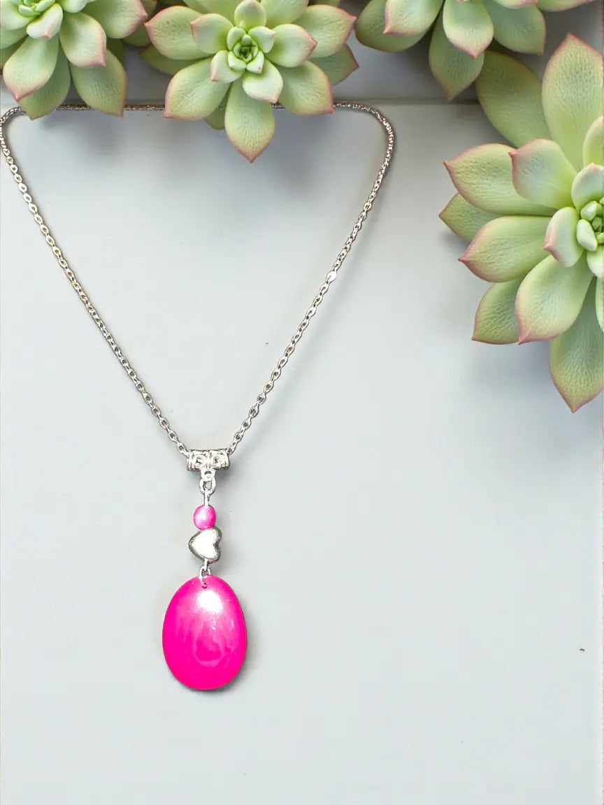 A vibrant pink tagua necklace with an oval pendant silver chain and fair trade heart bead charm from the rainforest