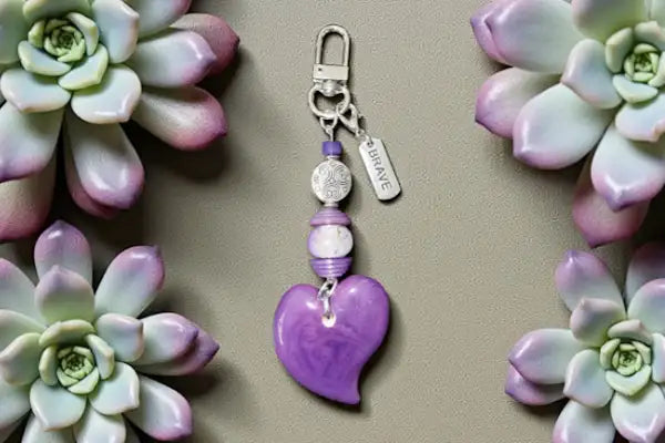 Purple heart-shaped charm with a silver-toned clasp and beads, featuring an engraved ’brace’ tag.
