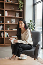 Woman wearing cream knit sweater and black pants seated with red drop perfect polished tagua sliced earrings