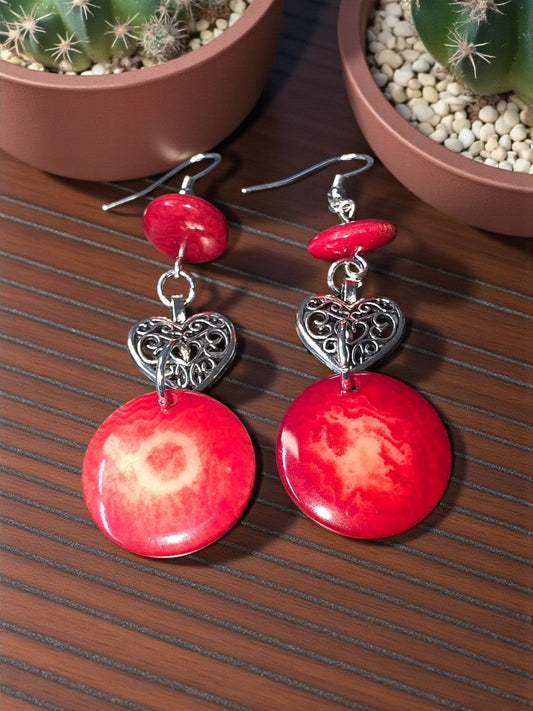 Red earrings with silver heart charms on a wooden surface with cacti in the background