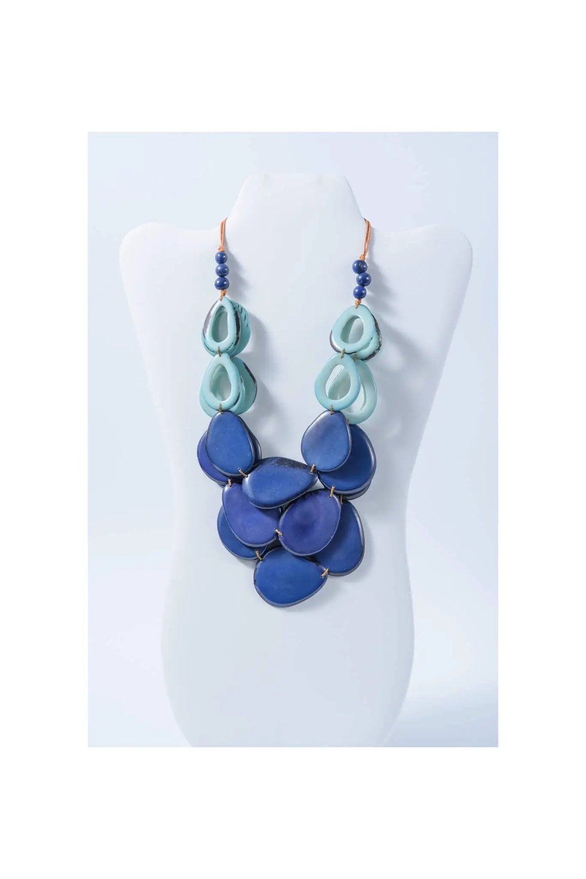 A layered remy vibrant tagua necklace featuring teal and deep blue teardrop beads with dark blue pearl loop accents