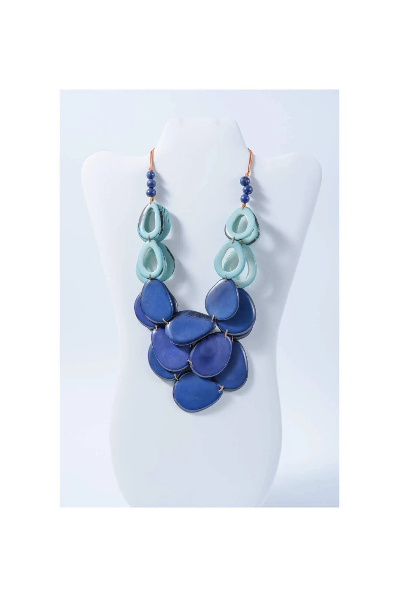 A layered remy vibrant tagua necklace featuring teal and deep blue teardrop beads with dark blue pearl loop accents