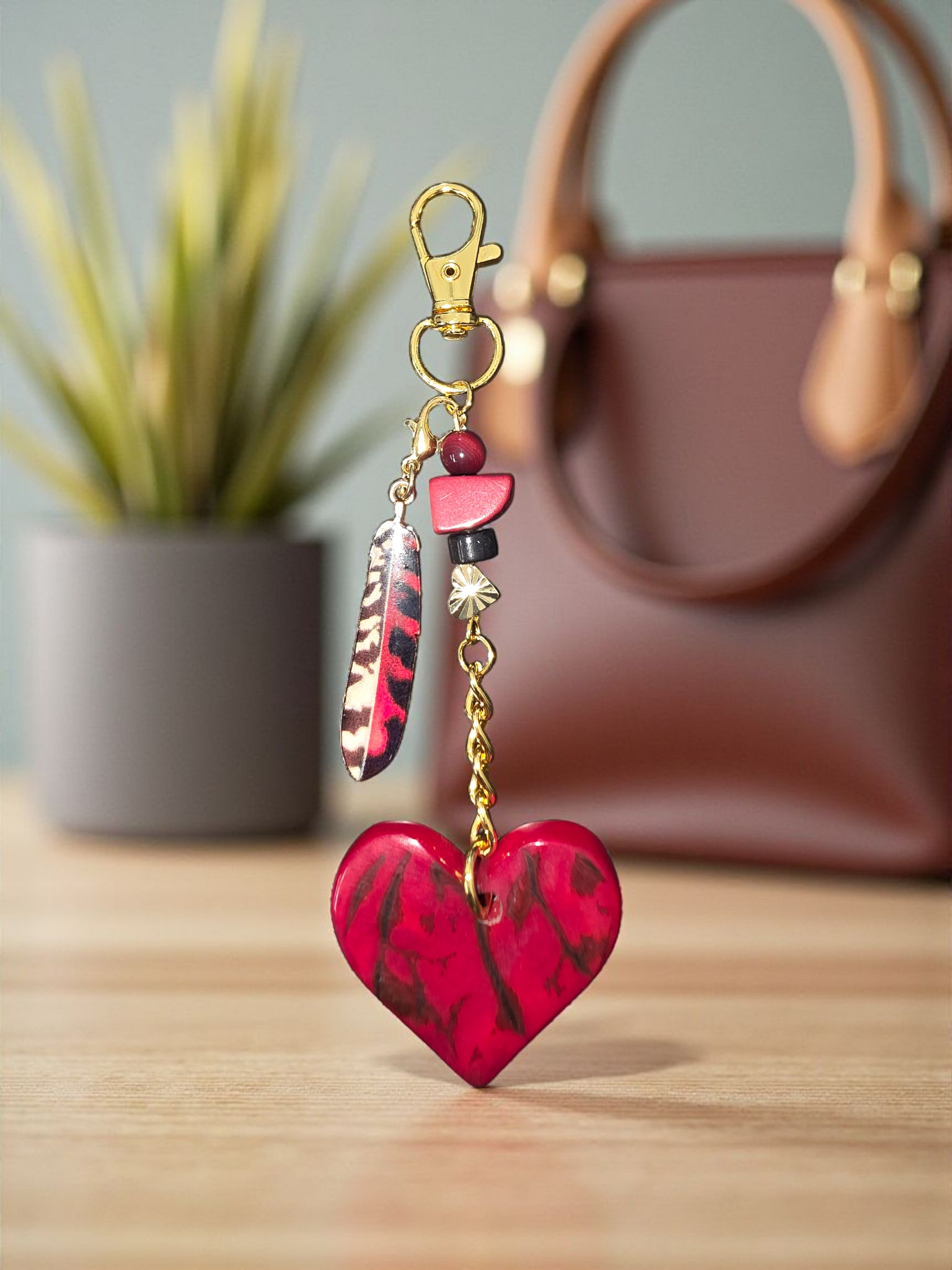 Red heart-shaped keychain with feathers on a wooden surface, blurred background
