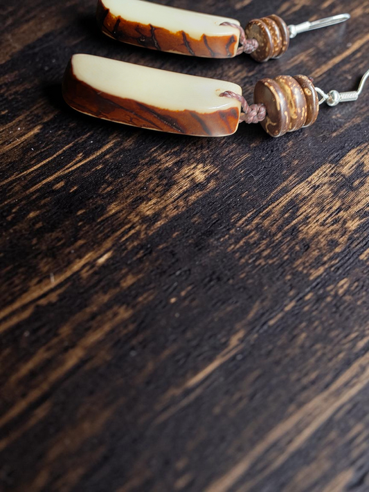 Tagua earrings with raw edge brown and white striped design on a dark wooden surface