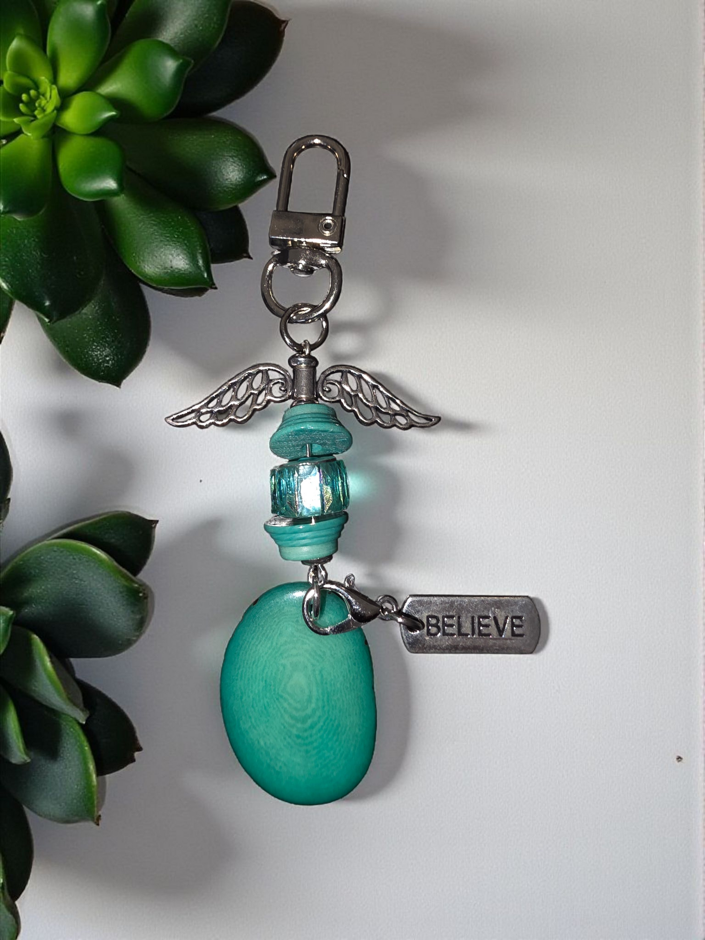 Turquoise keychain with angel wing charm and 'BELIEVE' tag against a white background