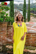 A vibrant yellow sleeveless maxi dress with a flowing fit and pastel multi floral embellishment at the neckline