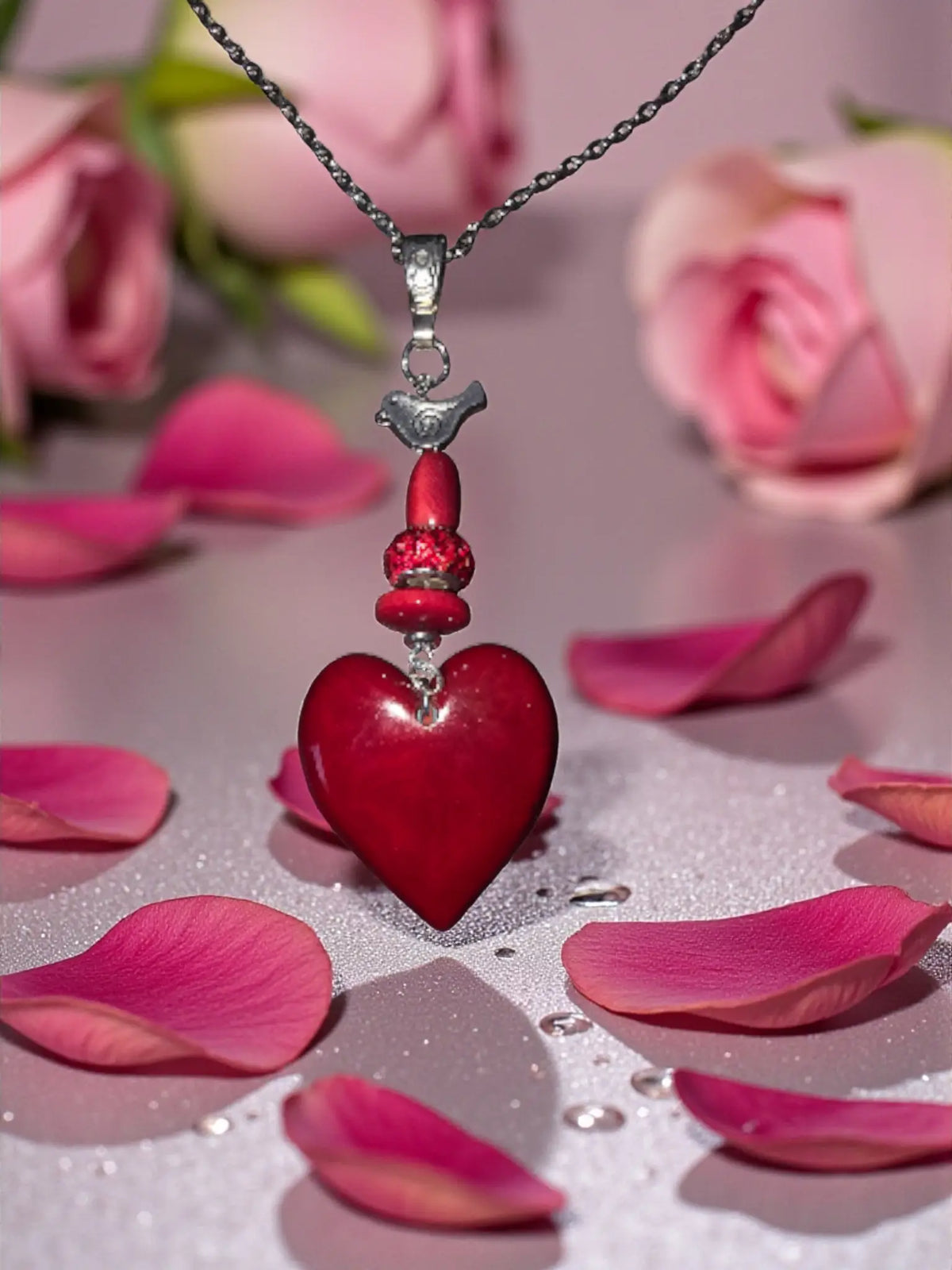 Ruby red carved tagua heart pendant necklace with a glossy red heart, silver bird charm, beaded accents, and fair trade design