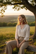 Woman wearing a cream-colored linen blouse with three-quarter sleeves and matching wide-leg trousers with red earrings
