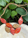 A samira necklace featuring vibrant hand-painted red orange and tan leaf pendants on a light brown leather cord