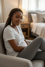 A woman with long braided hair wears simple cream fan tagua lightweight handmade earrings in a gray armchair