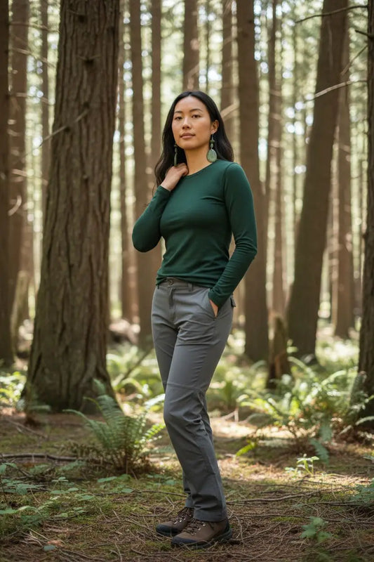 A woman wearing a stunning sage story grain top and cut tagua earrings stands in a forest setting