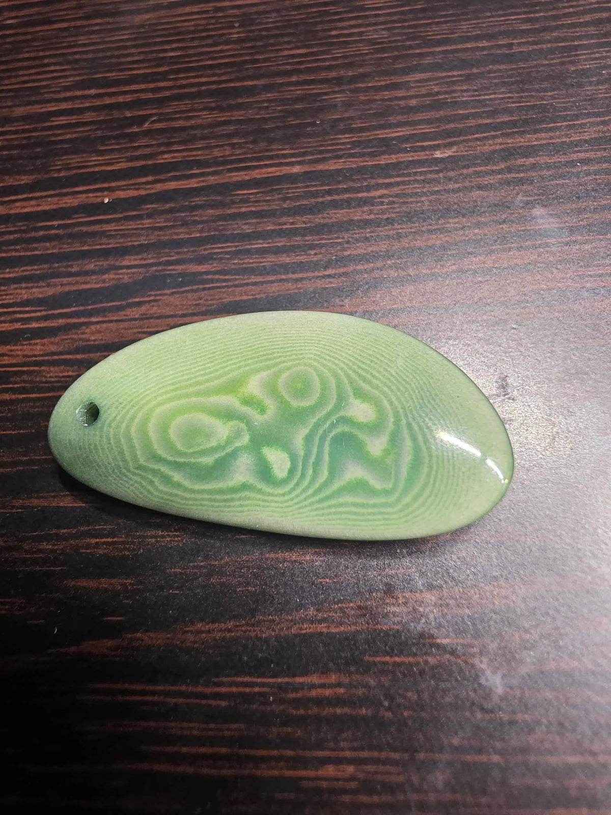 A smooth light green jade pendant with white swirls and a hole, complementing stunning sage story cut tagua earrings