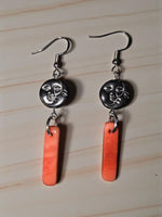 Silver dangle earrings with black moon face charm featuring two faces above orange peach melon tagua pendant