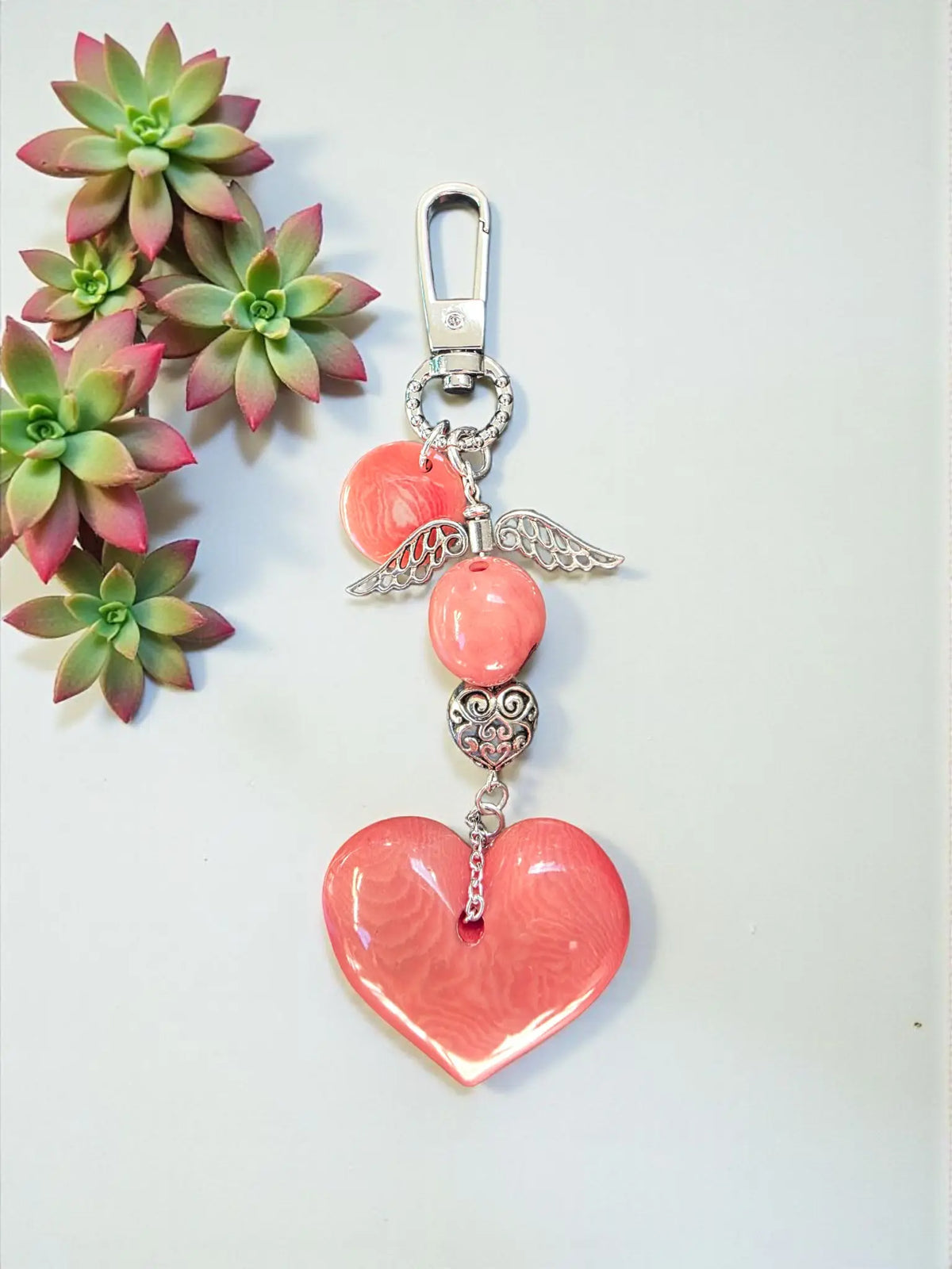 A coral-colored heart tagua bag charm with silver angel wing pendant and metal bead on metal clasp, vegan keychain