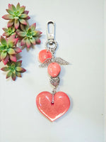 A coral-colored heart tagua bag charm with silver angel wing pendant and metal bead on metal clasp, vegan keychain