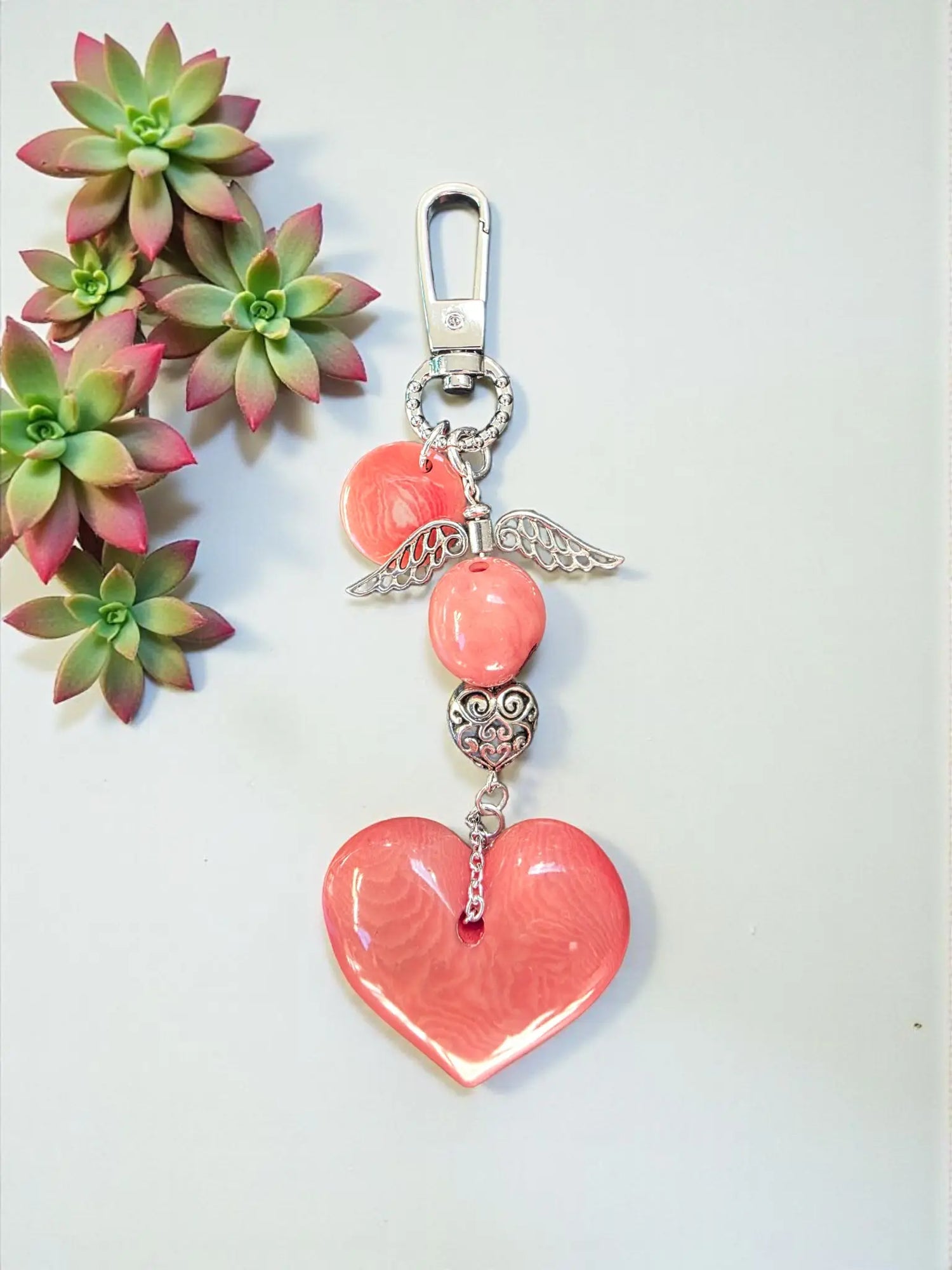 A coral-colored heart tagua bag charm with silver angel wing pendant and metal bead on metal clasp, vegan keychain