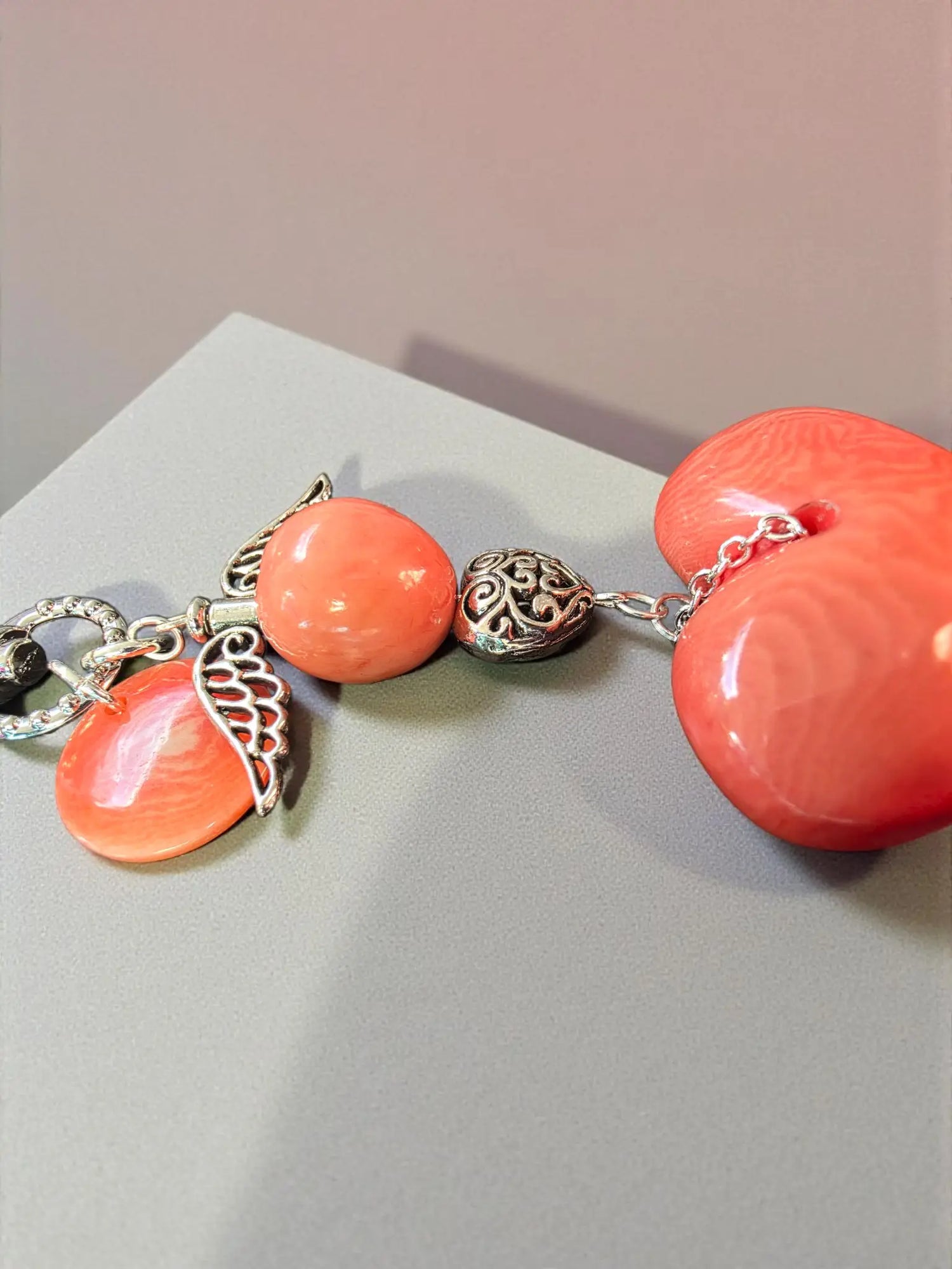 A coral-colored tagua heart bag charm with silver angel wing charms and an ornate metal bead vegan keychain