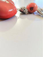 Coral-colored heart-shaped pendant necklace with silver filigree accents and matching chain displayed front view
