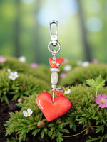 A vibrant red tangerine tagua carved heart bag charm with glossy finish silver clasp and ceramic folk art bird bead