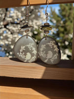 Gray tagua earrings engraved with delicate white bird and vine designs sweet songbird singing on a vine